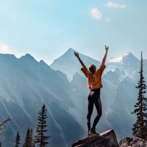 Vrouw op een bergtop die haar kracht en visie omarmt. | Woman on a mountain embracing her strength and vision.